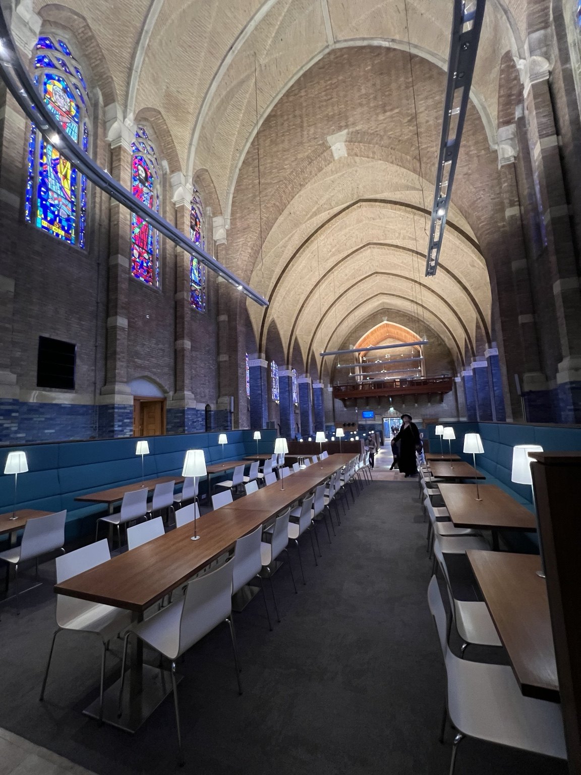 A view along the former chapel, with high brick arches, stained-glass windows, tables and modern lighting.